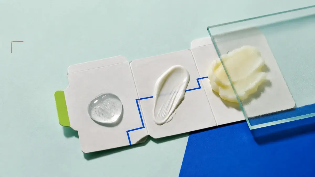 Gel, krem og tett balm på tre felt av en utfoldet kosmetikkartong under frostet glass